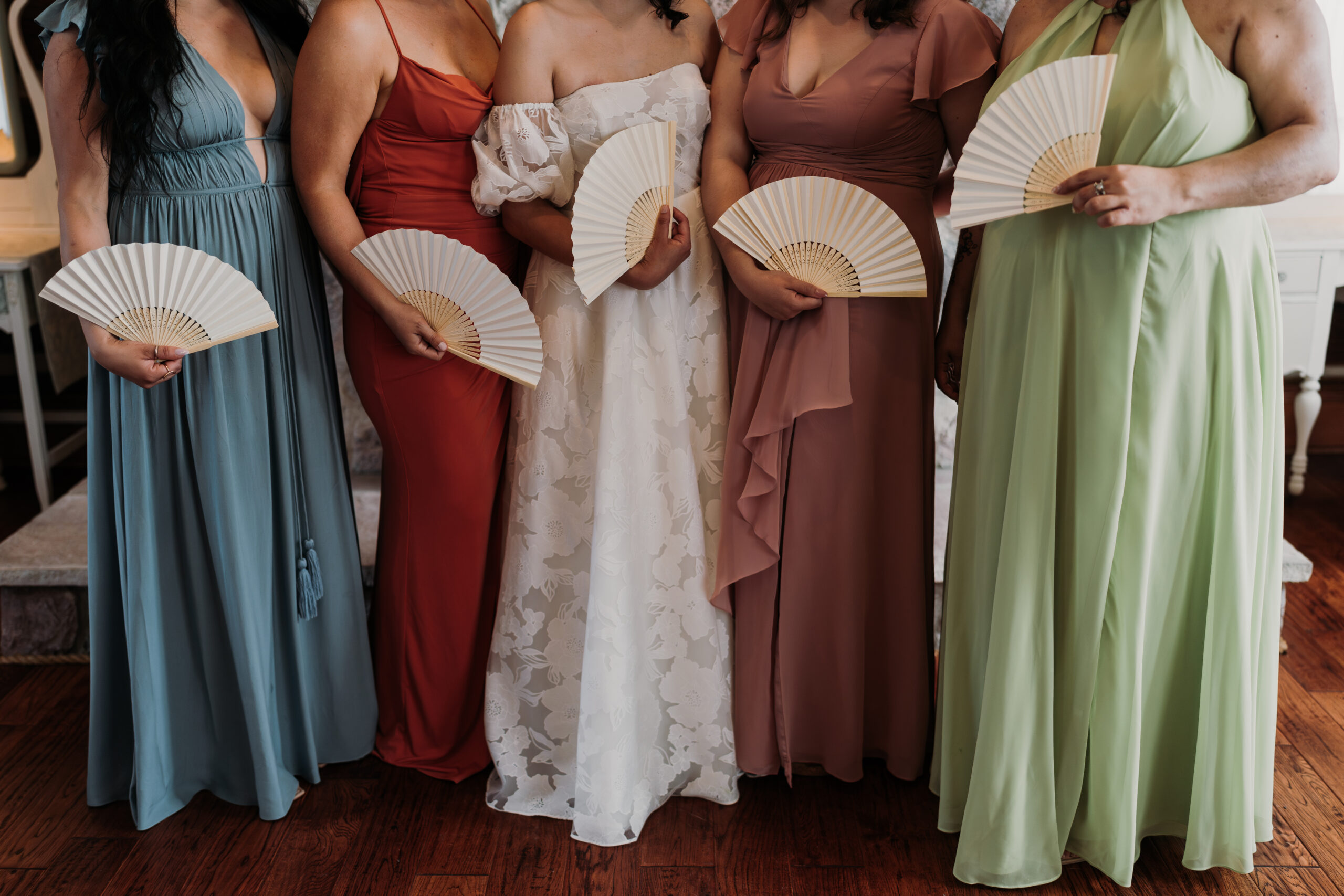 Mismatched bridesmaid dresses with handheld fans at a wedding at Stonefields Estate, captured by Lauren McCormick Photography.