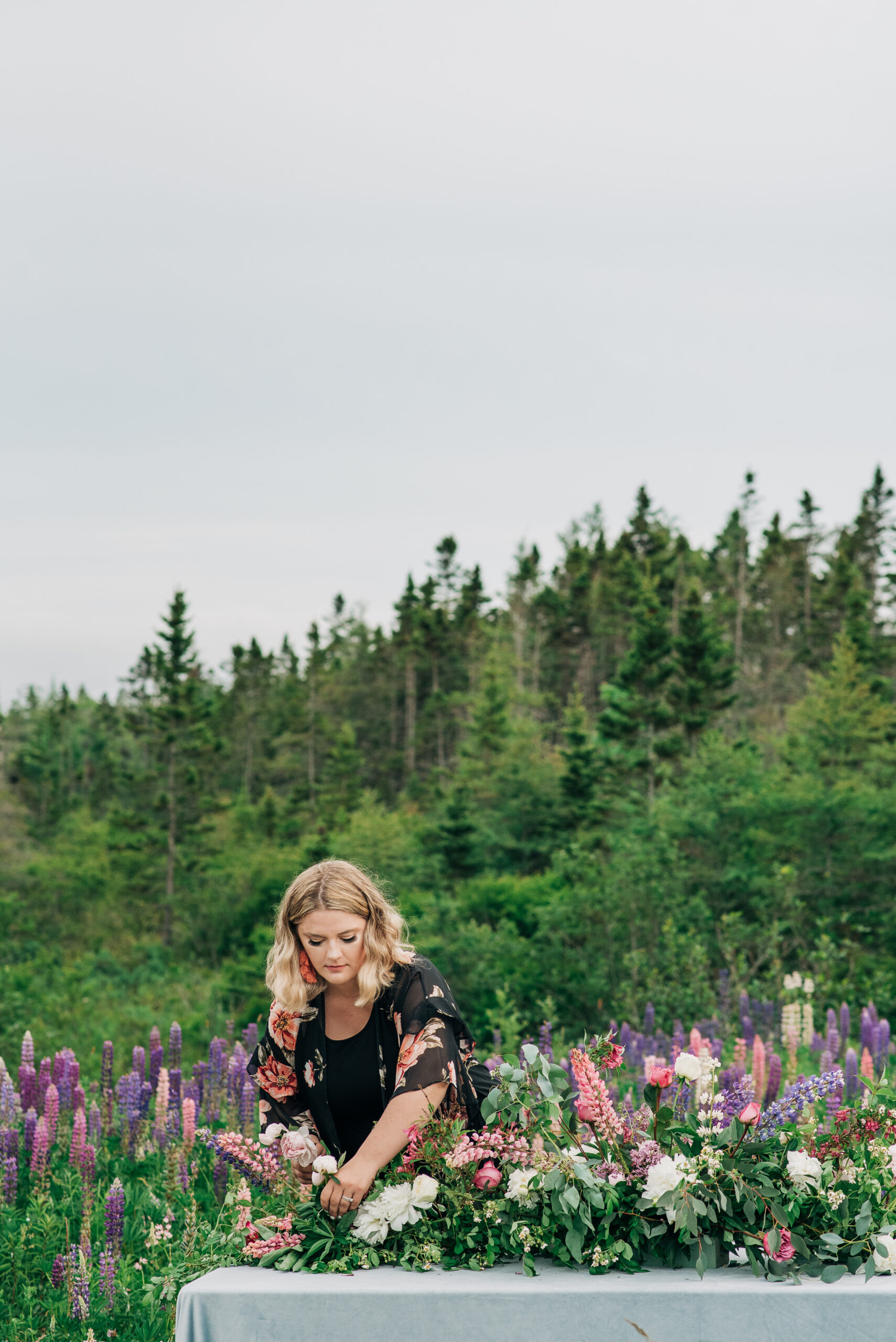 Brittany Bested standing in a field of vibrant lupins, embodying the elegance of a Claude Monet-inspired wedding tablescape. Captured by Chris and Amber Photography, this stunning portrait highlights the artistry and beauty of thoughtfully planned weddings.